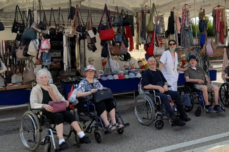 Cinque anziani in carrozzina davanti a una bancarella di borse