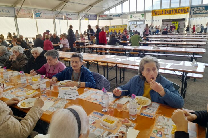 Tavolata di anziani che mangiano in compagnia sotto il tendone sagra del santo patrono