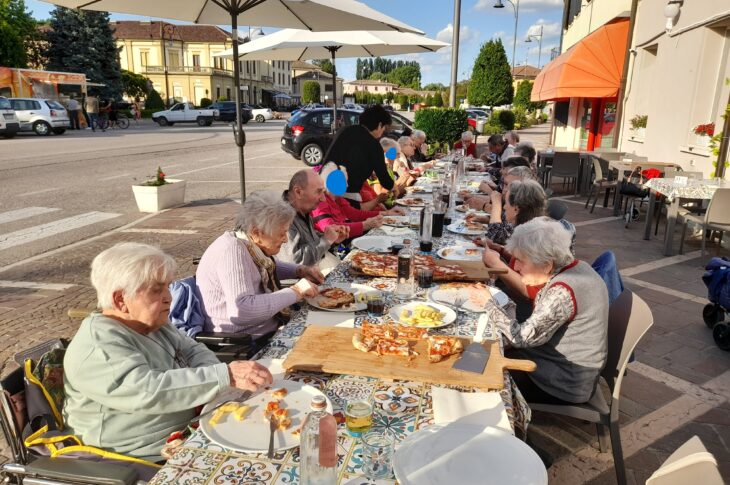 Gruppo di anziani pranza all’esterno sotto ombrelloni